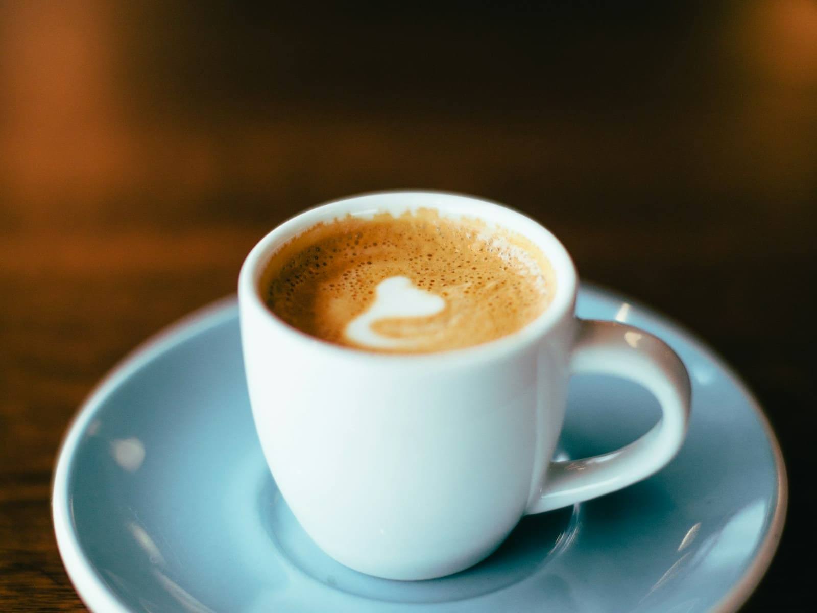 Cup of coffee with a heart in the foam on a pale blue saucer