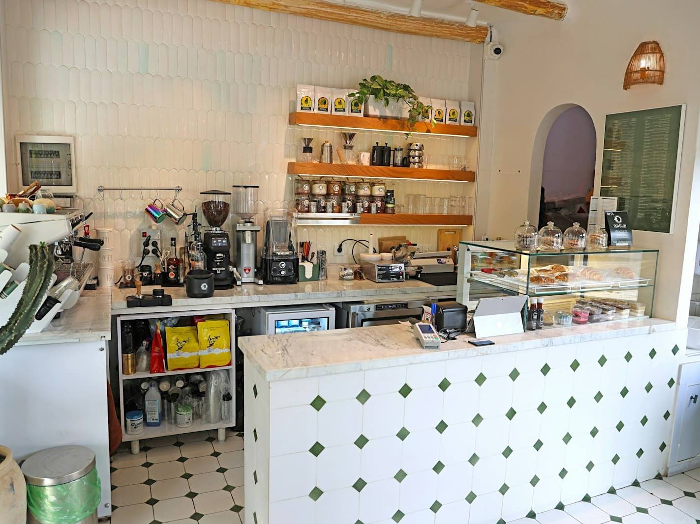 Bright café counter with a pastry cabinet and shelves of coffee gear