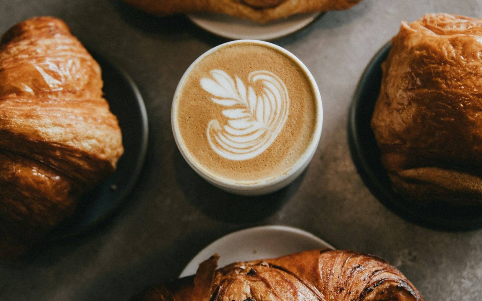 Flat white with latte art surrounded by croissants on a stone table