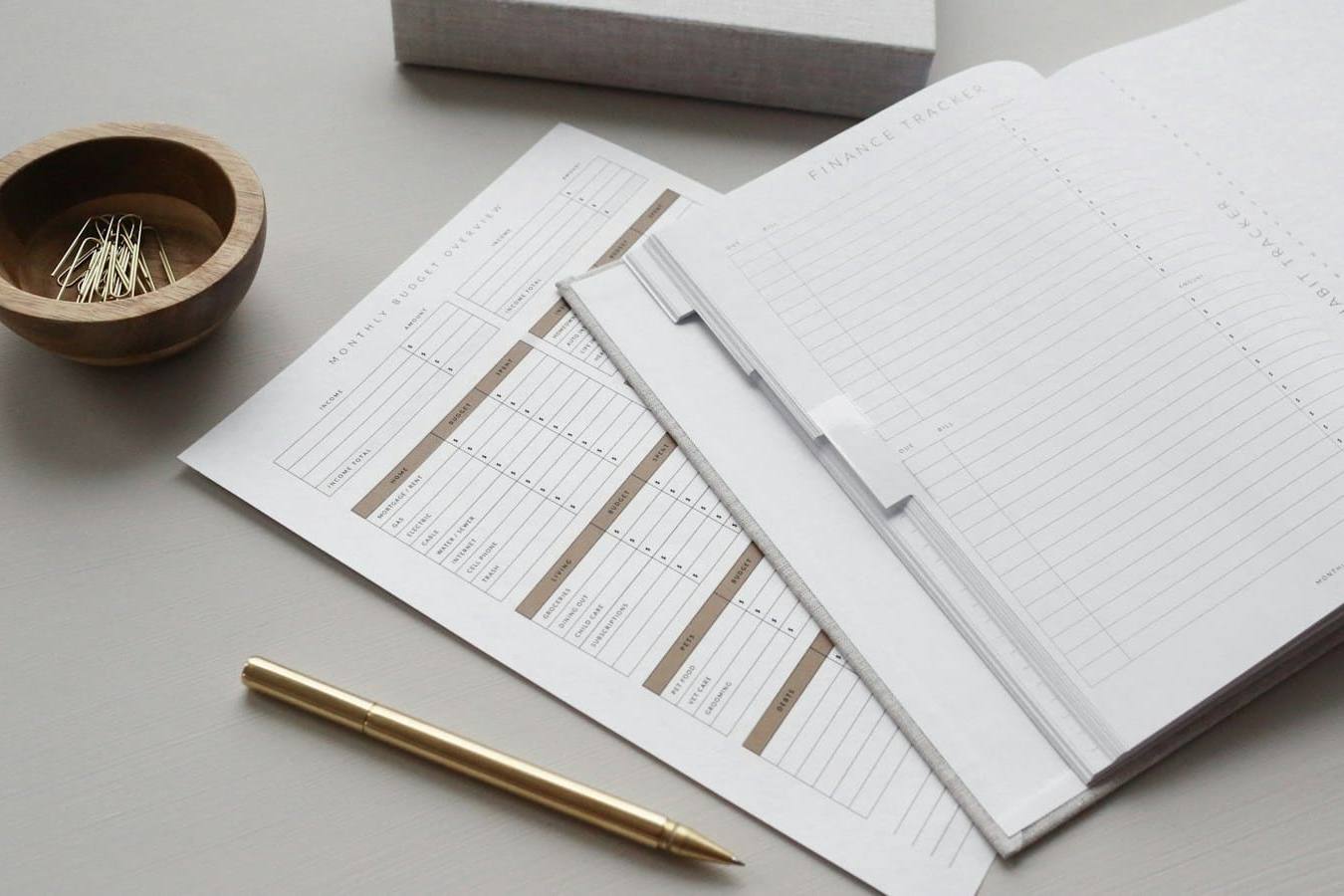Budget planner pages, a brass pen and paper clips on a grey desk