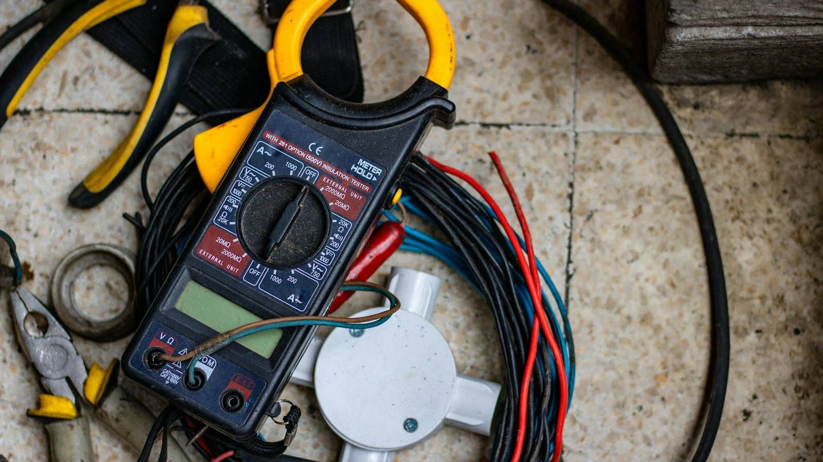 Clamp meter, pliers and coiled cable on a workshop floor