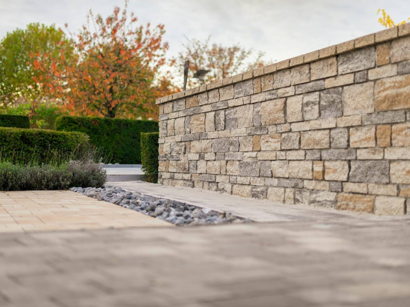 Sandstone-look block wall with paving and clipped hedges